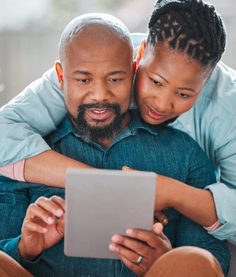 A Black man and woman embracing looking at a tablet