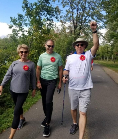 Trois personnes aînées portant l'épingle rouge de Myélome Canada marchent ensemble dans un parc