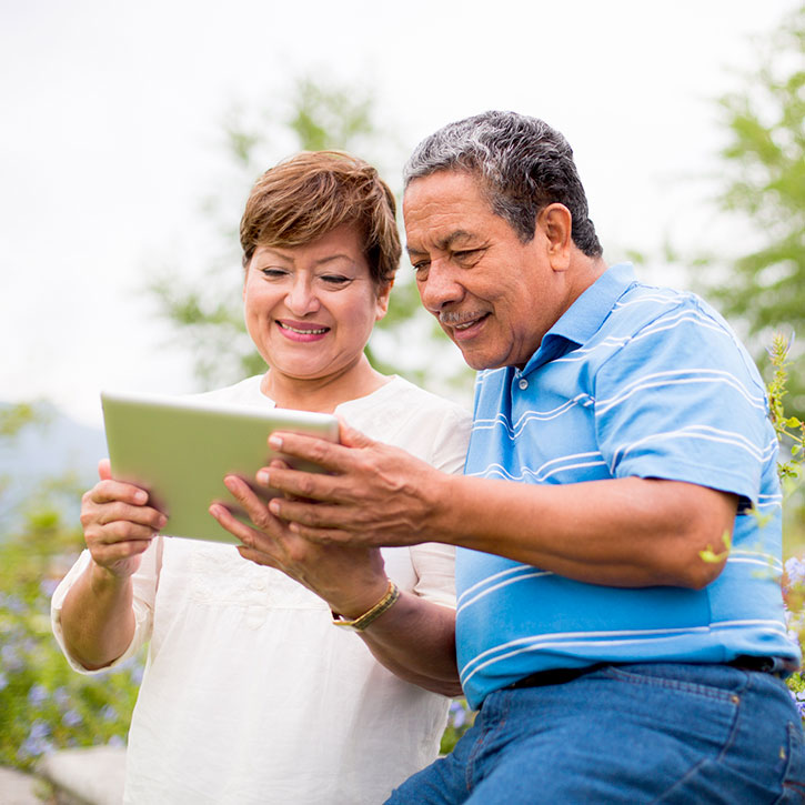 Un homme et une femme assis dans un jardin regardent à leur tablette électronique