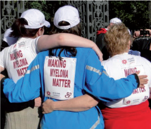 The backs of three women each wearing a Make Myeloma Matter bib, with their arms around eac hother