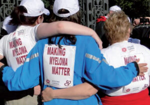 The backs of three women each wearing a Make Myeloma Matter bib, with their arms around eac hother