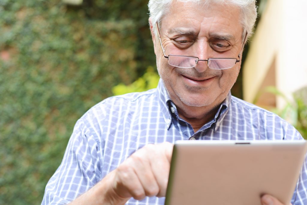 An older man with glasses smiling, pointing and reading on his tablet screen