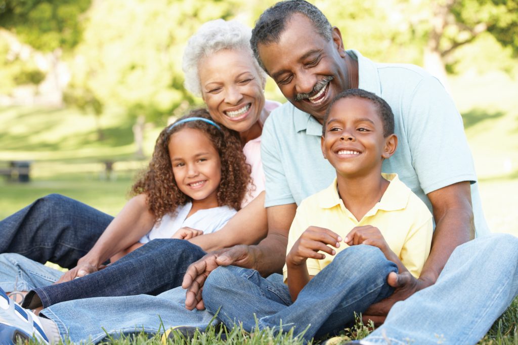 A Black family smiling and sitting in a park