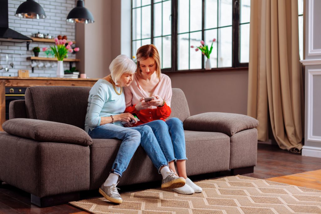 Young woman sitting on a sofa showing older woman something on a smart phone