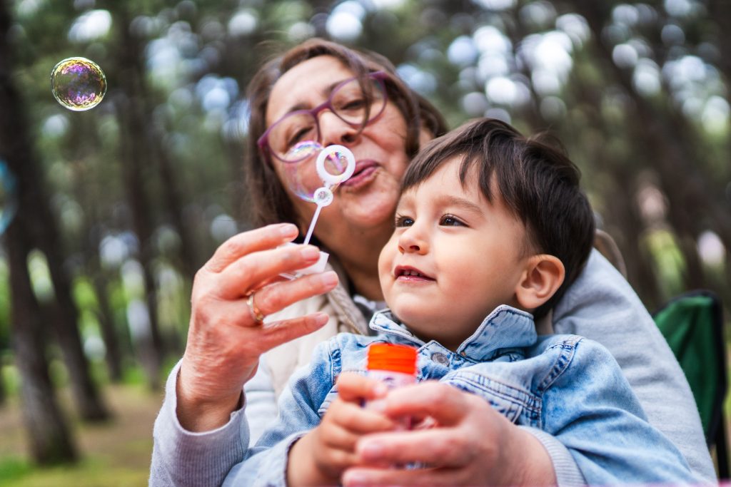 A child and an adult blowing bubbles outside and smiling