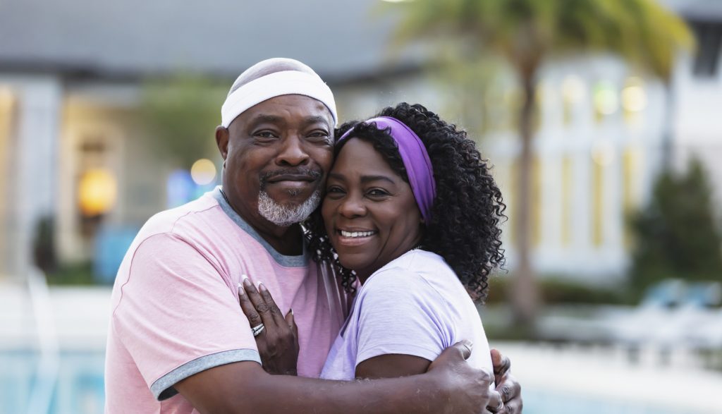 A Black couple smiling and hugging in front of a pool