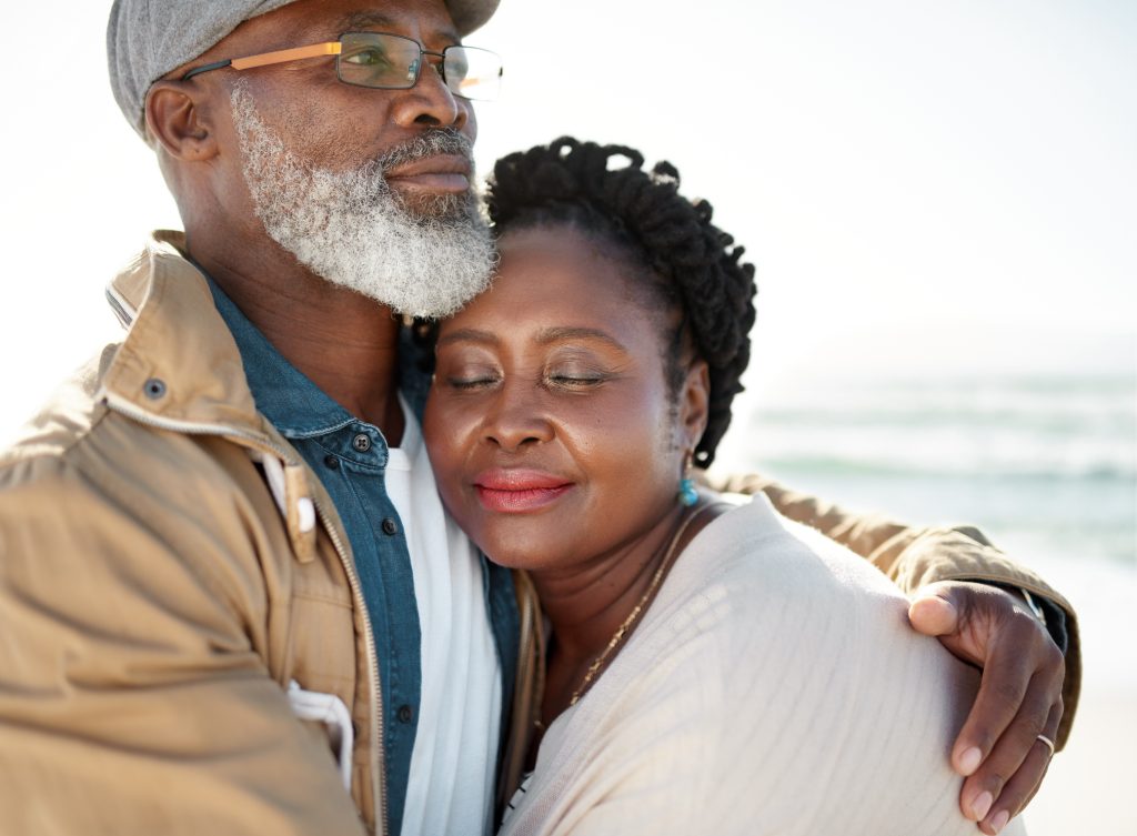 A greyed-hair Black man hugging a woman by the ocean
