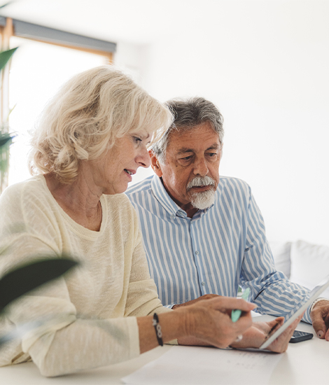 Une femme et un homme âgés discutent en regardant une tablette électronique tenue par la femme.