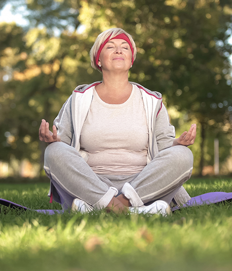 MIddle-aged white woman in lotus pose meditating in the park