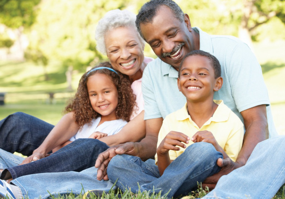 Happy Black grandparents and their grandchildren sitting in the grass.