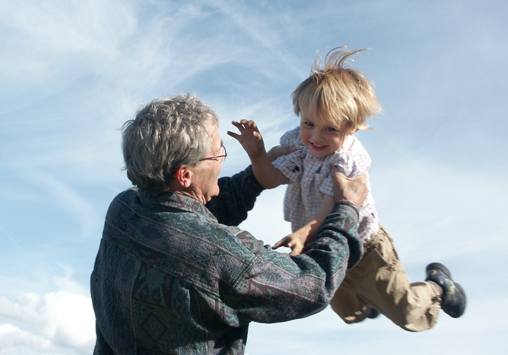 A grandfather playfully throws his young grandson in the air