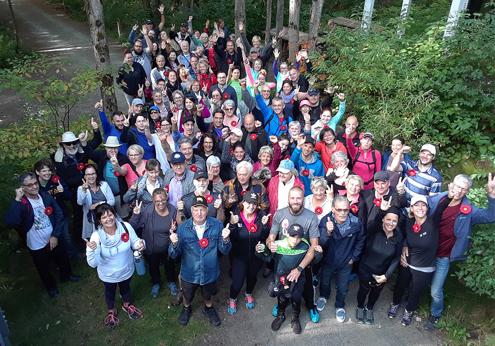 Photo of a large group of happy people gathered in a forest wearing the Myeloma Canada pin before the Multiple Myeloma March