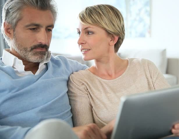 A middle-aged white couple discuss something and look at their digital tablet