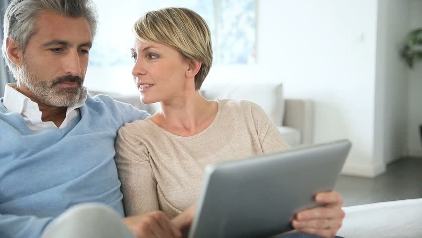 Un homme et une femme d'âge moyen discutent en regardant une tablette électronique.