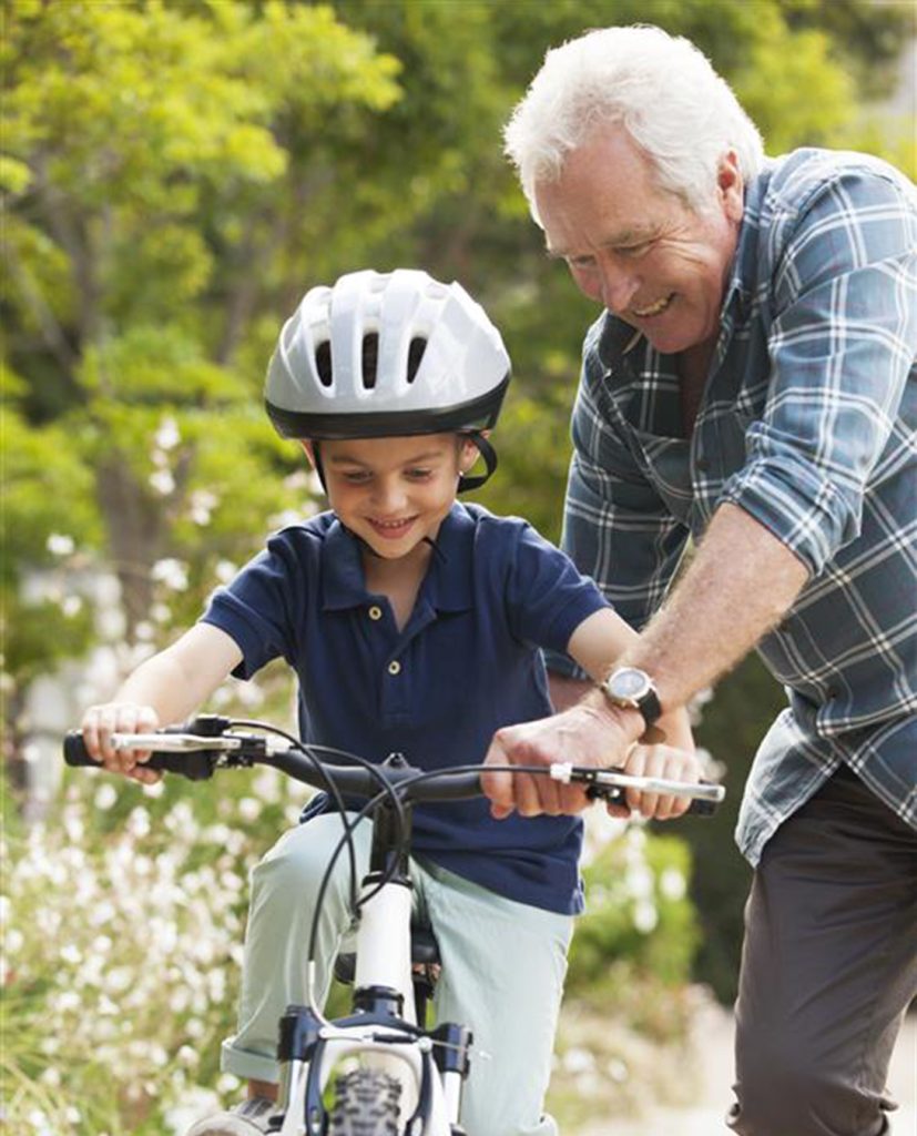 A grandfather teaches his young grandson to ride a bicycle