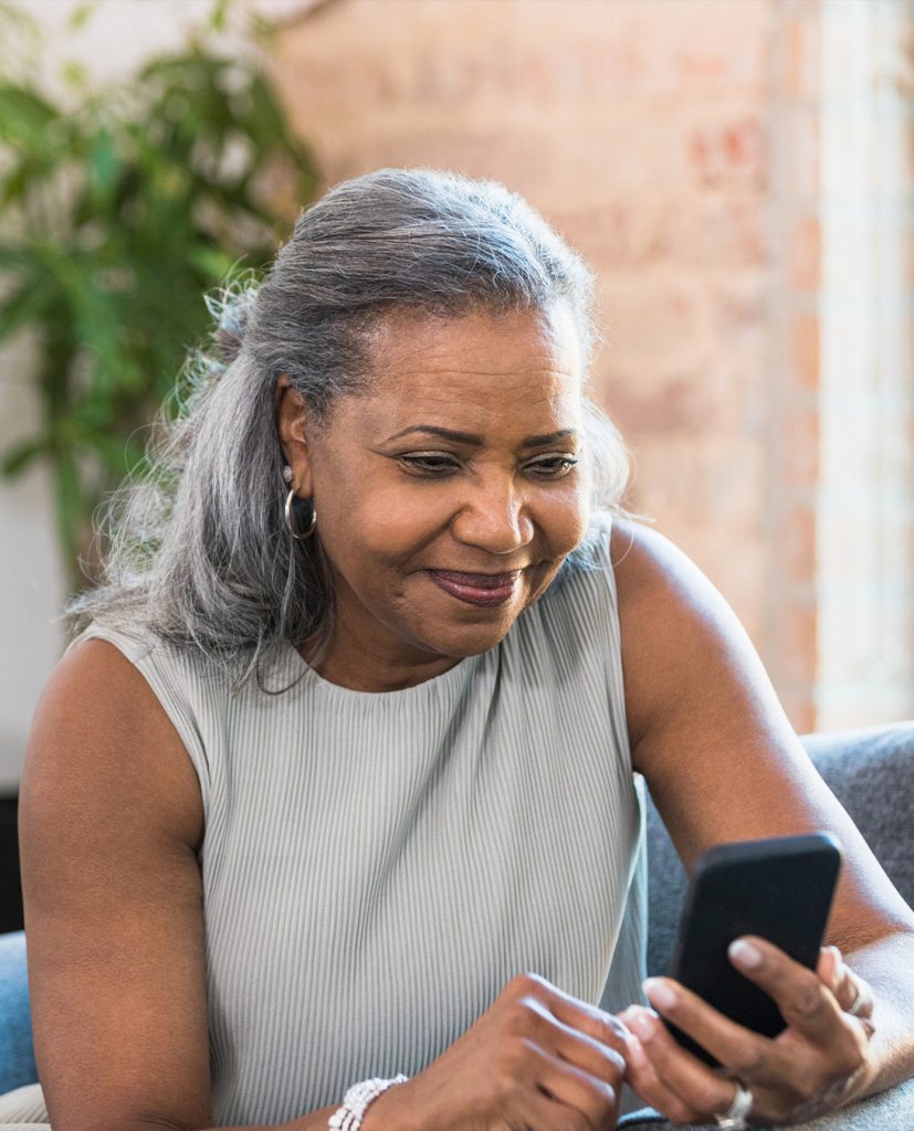 Une femme âgée noire sourit en utilisant son téléphone portable.