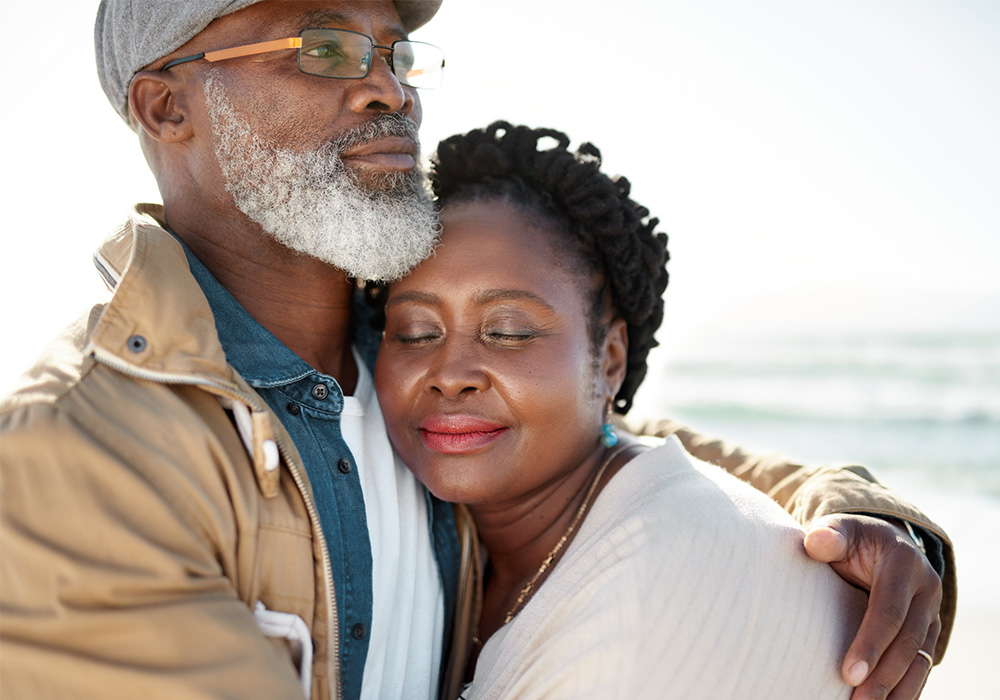 Un homme noir aux cheveux gris enlace sa femme au bord de la mer