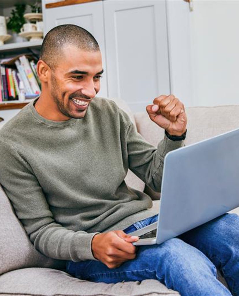Un homme noir utilise un ordinateur portable avec un grand sourire et le point dans les airs.