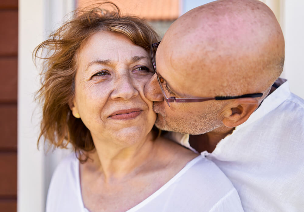An older bald man kissing his wife on the cheek