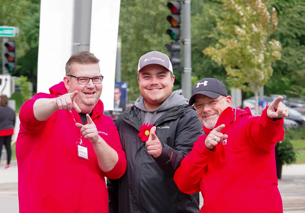 Three men wearing the Myeloma Canada flower and colours point excitedly at the Multiple Myeloma March in Quebec City, QC